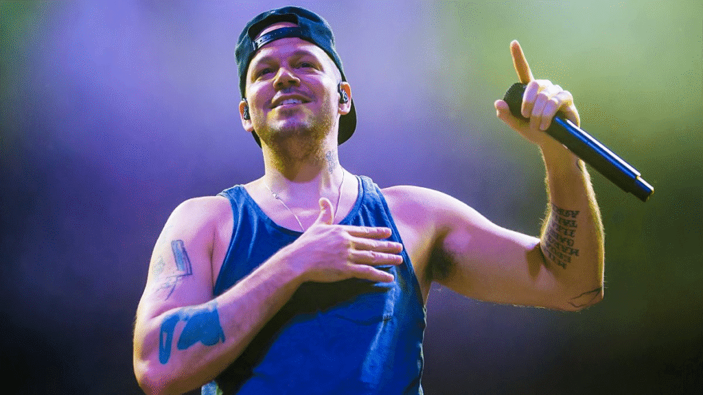 Residente dará concierto gratis en el Zócalo de CDMX 6 El rapero Residente actuando en un concierto, con una sonrisa y un micrófono en la mano, vistiendo una camiseta sin mangas y una gorra.