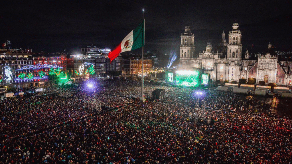 Residente dará concierto gratis en el Zócalo de CDMX 7 Amplia vista del Zócalo de la Ciudad de México durante un concierto, con una gran multitud reunida bajo un cielo nocturno iluminado y una bandera mexicana ondeando.