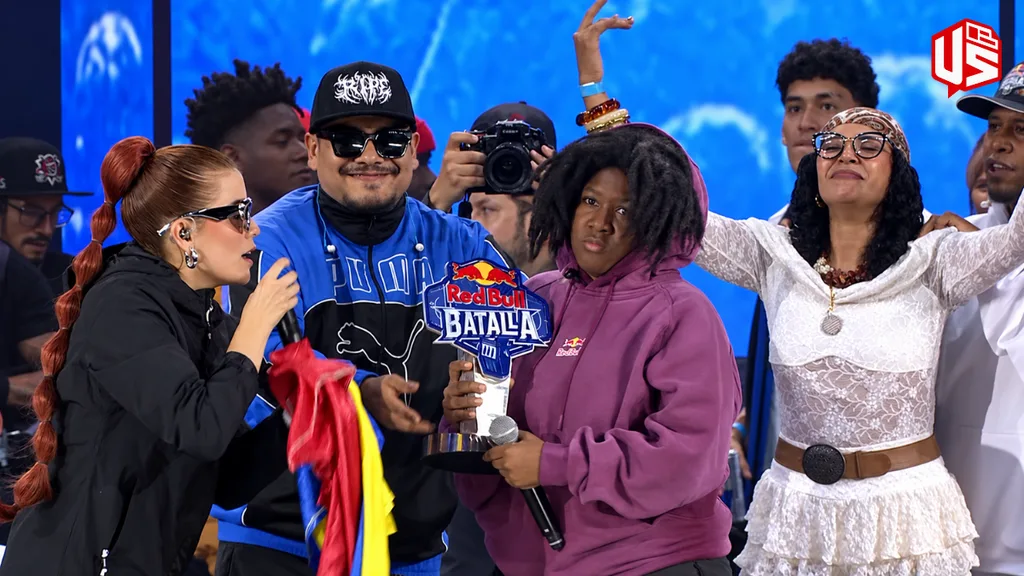 Marithea es bicampeona de Red Bull Batalla Colombia 2026 Marithea sostiene el trofeo de Red Bull Batalla Colombia 2026 y un micrófono en el escenario, con una sudadera morada de Red Bull, rodeada de personas que celebran